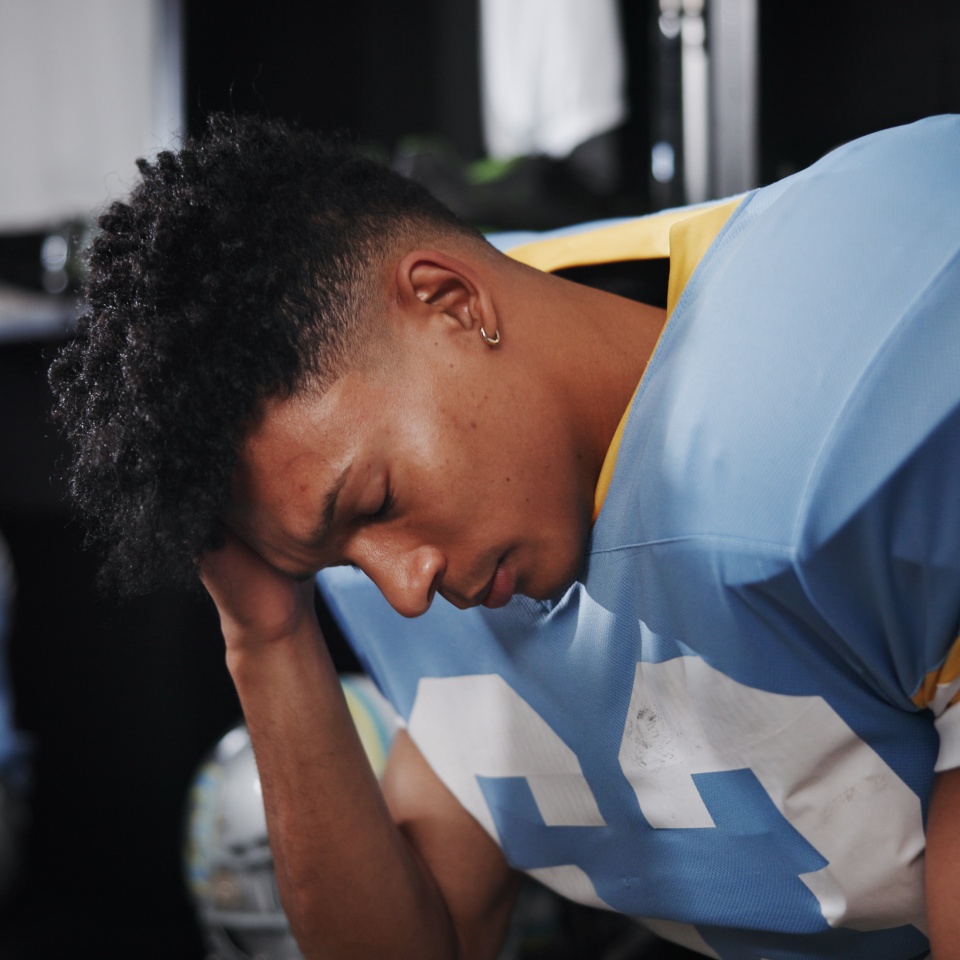 Man, American football player and headache with stress in locker room, frustrated or concussion with sport injury. Person, migraine and professional athlete with cte, tired and burnout at franchise.