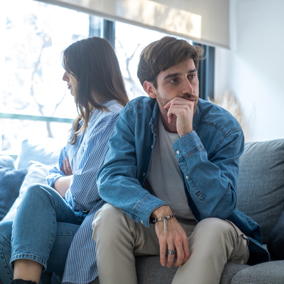Engaged couple with relationship problems sitting on the sofa with their backs to each other after an argument, conflicts in marriage, upset couple after a dispute, making decision to break up and divorce