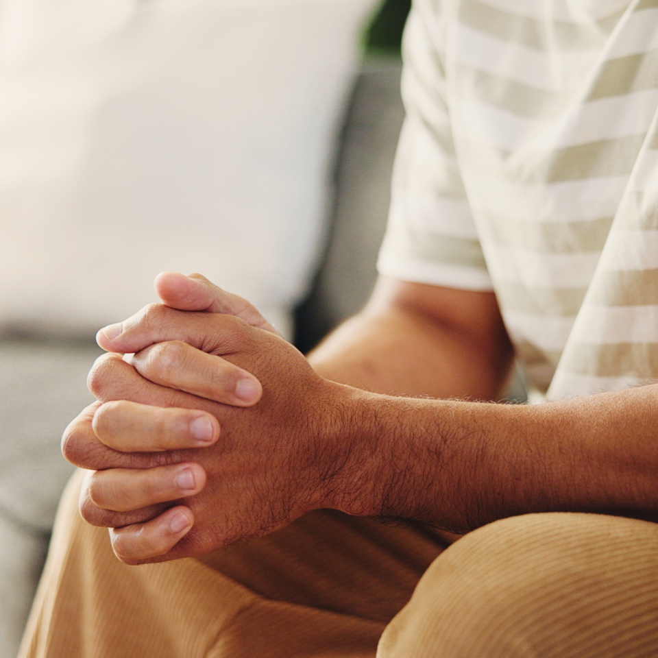 Hands, trauma and man on sofa in home with stress, phobia or stimming for panic attack with mental health. Overthink, crisis and male person in living room with anxiety, fear or trigger in house