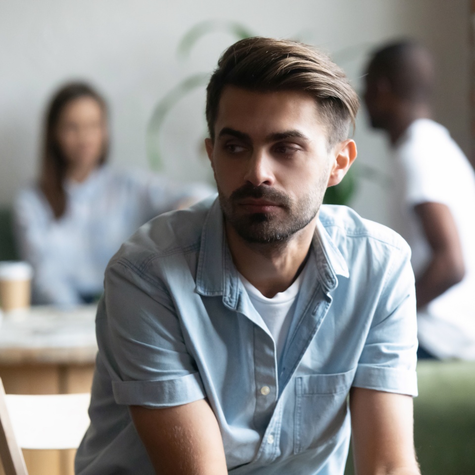 Different friends sitting in cafe after study spending time together, focus on frustrated lonely shy guy sitting apart, separately of others teenagers feels unhappy having problems with communication