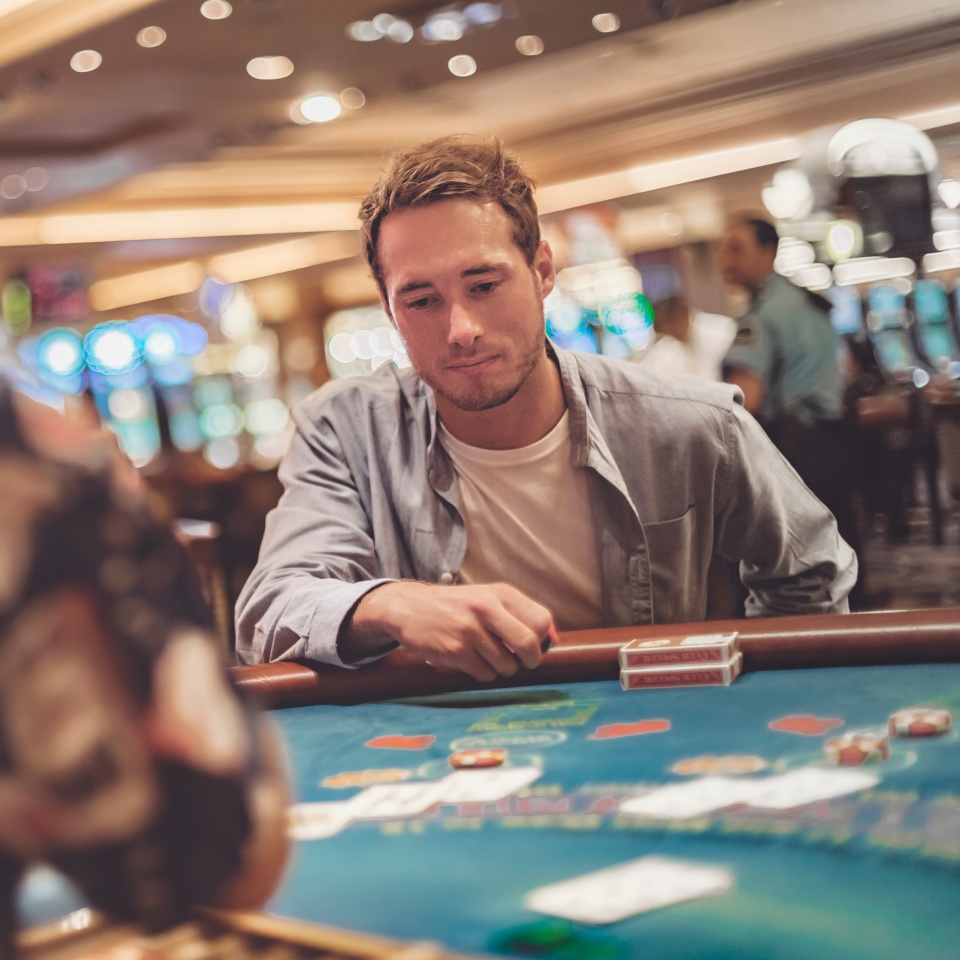 Casino gambling young man playing blackjack at table with cards and chips. Indoor portrait of gambler with dealer.