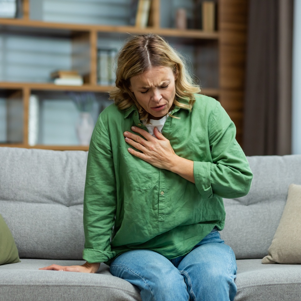Senior beautiful woman sitting sick on sofa at home. Holds his chest. He has asthma, allergies, feels severe pain, tenderness, panic attack, infarct.