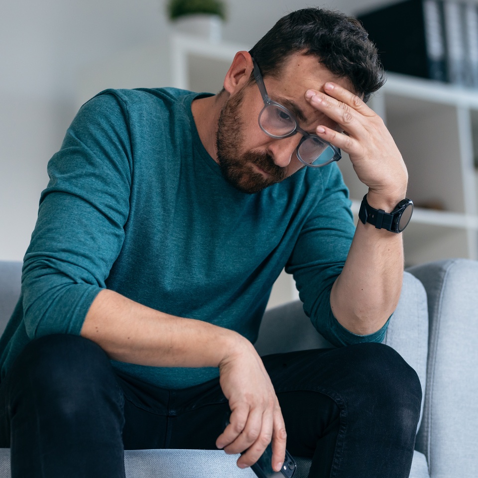 Shot of worried mature man thinking about what he has read on his mobile phone while sitting on the couch at home
