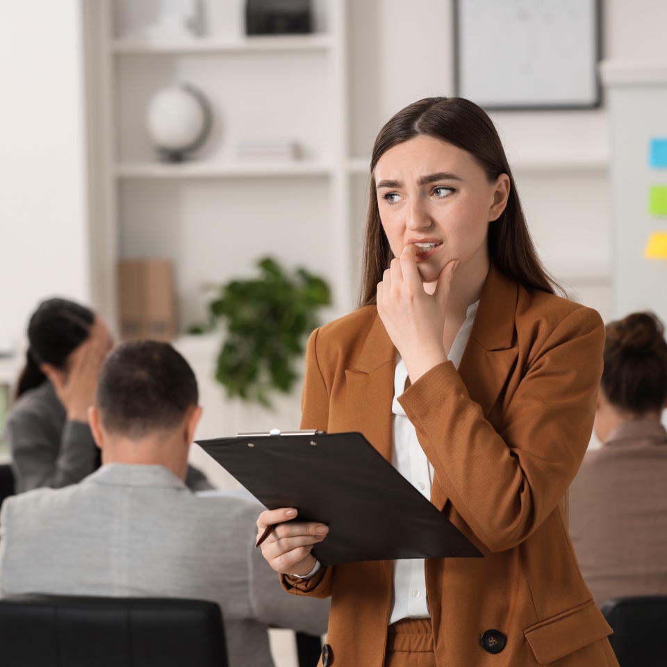 Woman with clipboard feeling embarrassed during business meeting in office